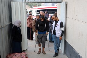 En man på kryckor leds in genom en dörr av en man med Läkare Utan Gränser väst.